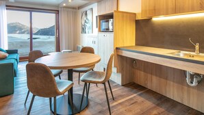 A modern kitchen with wooden cabinets, a dining area with a round table and chairs, and a view of a snowy landscape through a large window. - Group Mountain Stay for Six in Doucy (La Léchère)