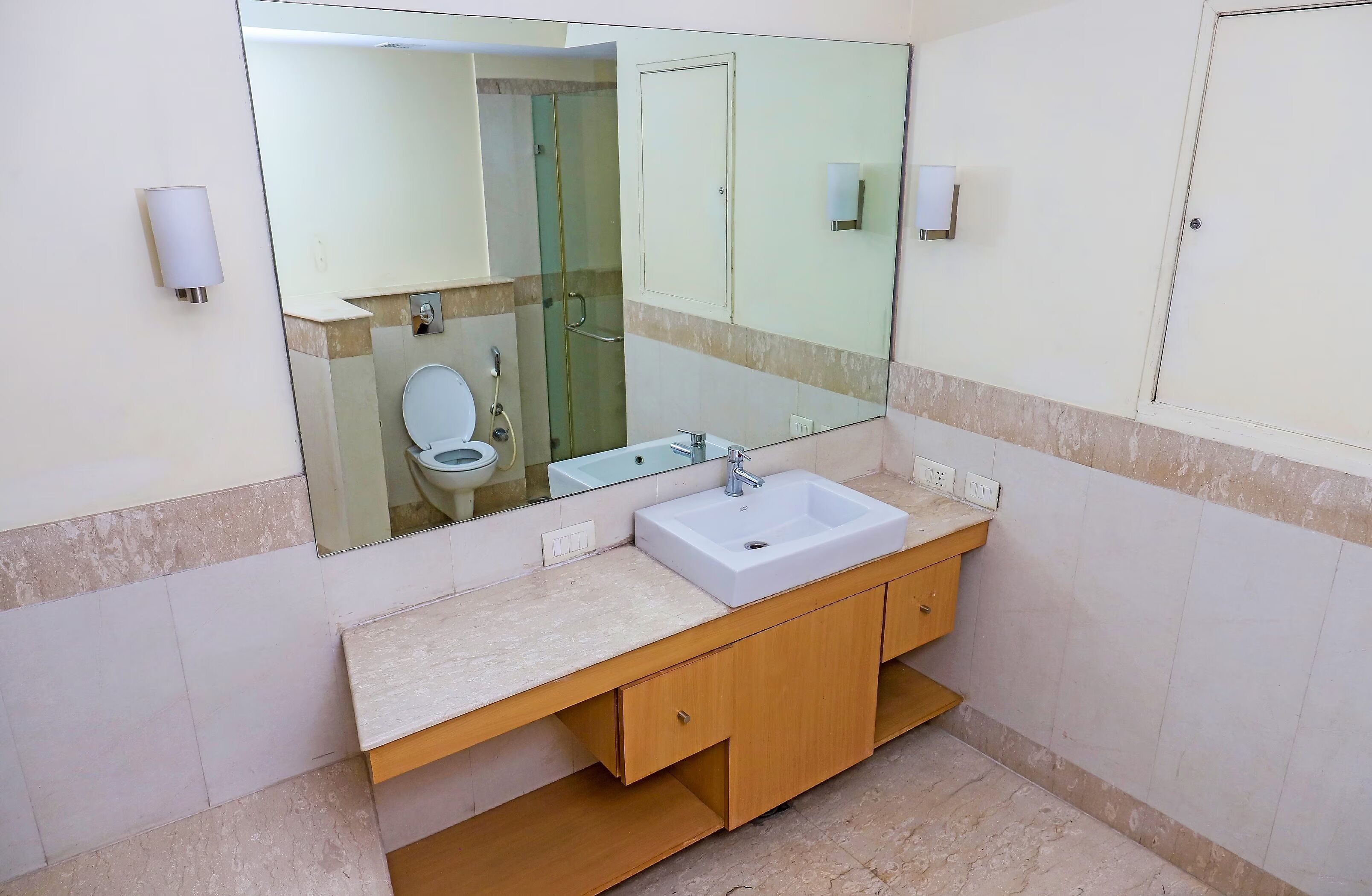 A bathroom with a large mirror, a white sink, wooden cabinets, and a glass shower enclosure.