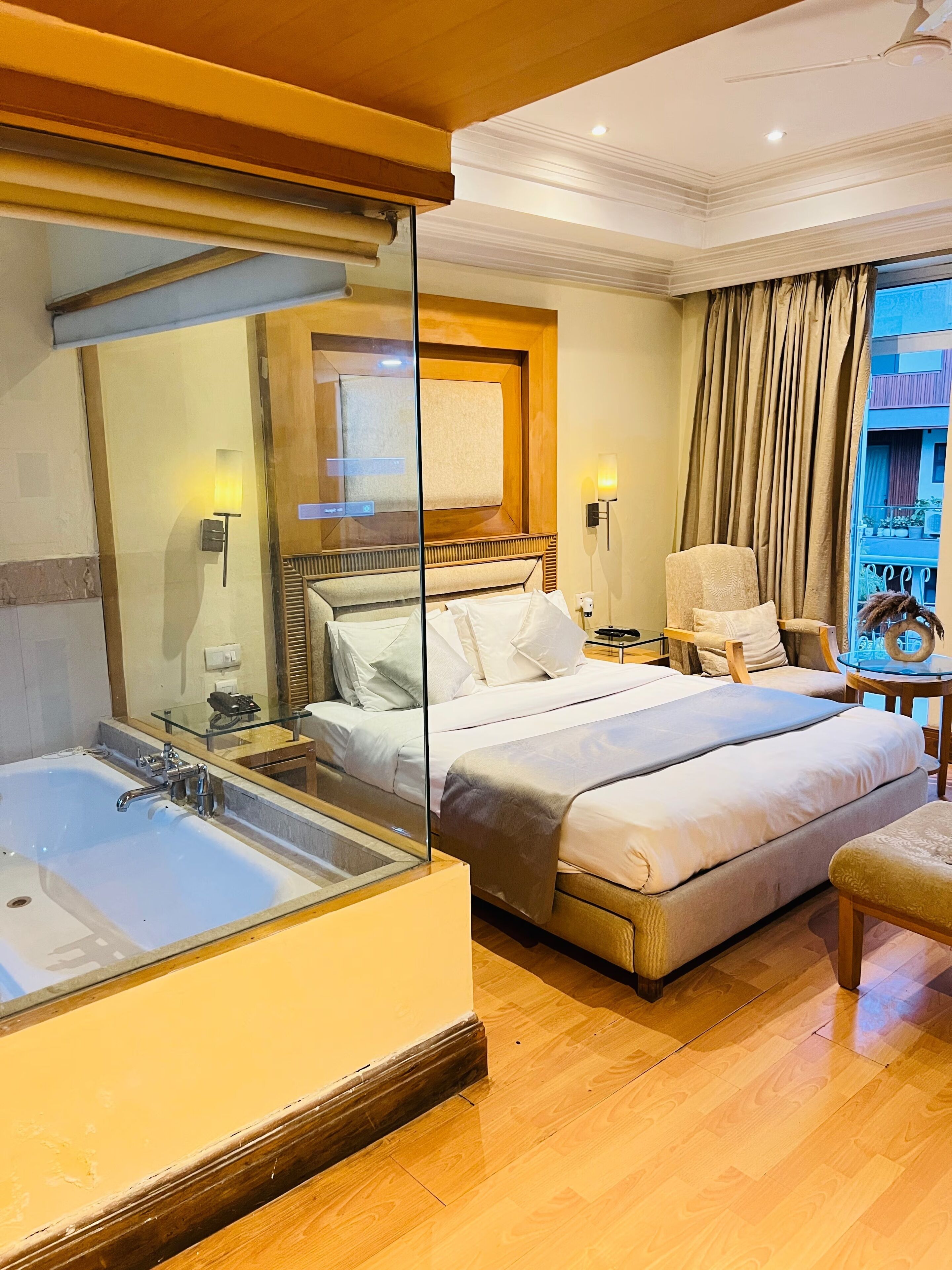 A hotel room with a large bed, a separate sitting area, a bathtub, and a view of the outside.