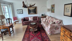 A living room with a wooden coffee table, two sofas, a patterned rug, and a chandelier. - Garden Villa Schwanstein I Apartment "Lohengrin" (Füssen)