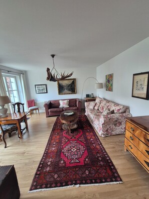 A living room with a wooden coffee table, two sofas, a patterned rug, and a chandelier. - Garden Villa Schwanstein I Apartment "Lohengrin" (Füssen)
