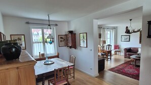 A spacious living area with a dining table, wooden flooring, and a red rug. - Garden Villa Schwanstein I Apartment "Lohengrin" (Füssen)