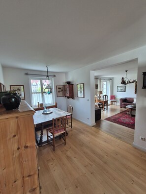 A spacious living area with a dining table, wooden flooring, and a red rug. - Garden Villa Schwanstein I Apartment "Lohengrin" (Füssen)