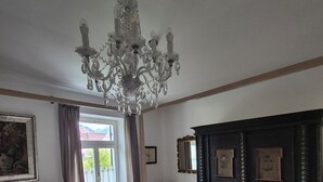 A bedroom with a chandelier, wooden furniture, a large mirror, and a window with curtains. - Garden Villa Schwanstein I Apartment "Lohengrin" (Füssen)