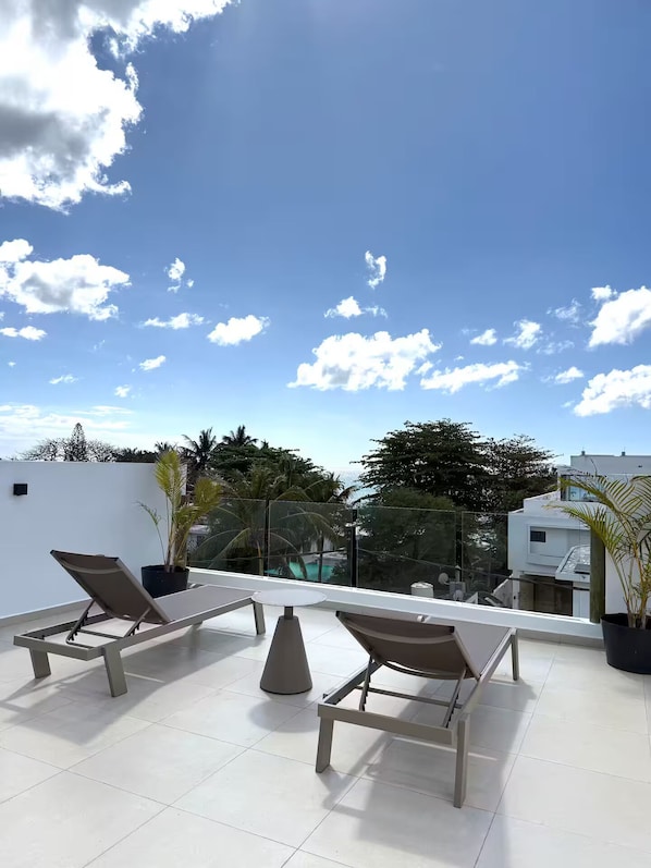 Eine Dachterrasse mit zwei Liegestühlen, einem kleinen Tisch und Topfpflanzen.