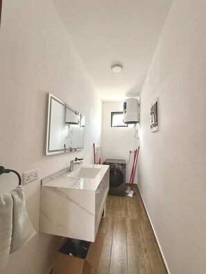 Ein modernes Badezimmer mit einem weißen Waschtisch, einem großen Spiegel, einer Waschmaschine und einem kleinen Fenster.