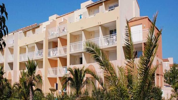 A multi-story hotel with balconies, palm trees, and a clear sky. - Golfside Apartment With Terrace (Agde)