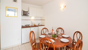 A dining area with a round table, six wooden chairs, a white cabinet, a microwave, and a small window. - Golfside Apartment With Terrace (Agde)