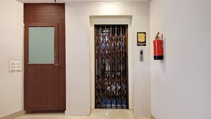 A hallway with a brown door, a metal gate, a fire extinguisher, and a sign on the wall. - Super OYO Collection O Jagadamba Junction Near Beach Road (Visakhapatnam)