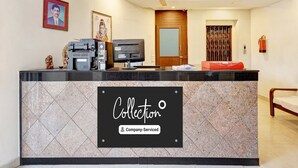A reception desk with a sign reading 'Collection Company-Serviced.' There are ceiling fans, a fire extinguisher, and a framed picture on the wall. - Super OYO Collection O Jagadamba Junction Near Beach Road (Visakhapatnam)