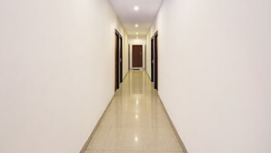 A long, narrow hallway with white walls and a shiny tiled floor, leading to a door at the end. - Super OYO Collection O Jagadamba Junction Near Beach Road (Visakhapatnam)