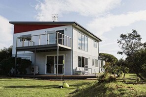 A modern two-story house with a balcony, large windows, and a well-maintained lawn. - Beach Haus Falmouth - Family Friendly Holiday Home (Break O'Day)