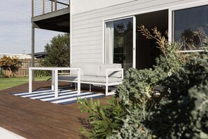 A modern house with a deck, a white outdoor seating area, and a large sliding glass door. - Beach Haus Falmouth - Family Friendly Holiday Home (Break O'Day)