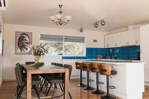 A modern kitchen with a central island, bar stools, and a dining table with chairs. - Beach Haus Falmouth - Family Friendly Holiday Home (Break O'Day)