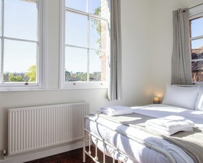 A bedroom with a bed, a radiator, and two windows with curtains. - 3 Bed Home in Shrewsbury (Shropshire)