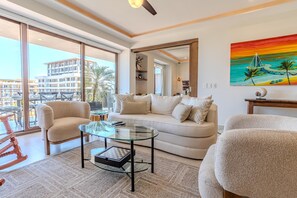 Ein modernes Wohnzimmer mit einem Glastisch, beigen Sofas und einem großen Fenster mit Blick auf ein Gebäude.