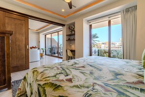 Ein Schlafzimmer mit einem großen Bett, einer Schiebetür zu einem Balkon und Blick auf Gebäude.