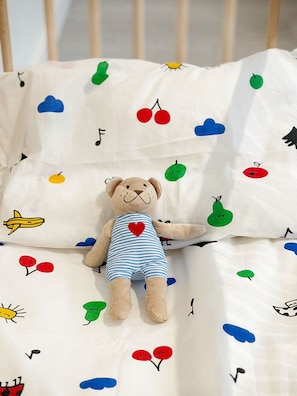 Una cama con un peluche y una sábana blanca con motivos de frutas y notas musicales.