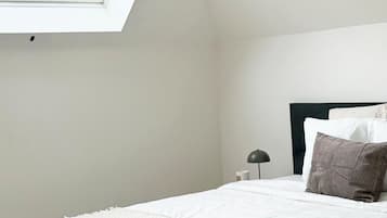A bedroom with a skylight, a bed with white bedding, a dark headboard, and a nightstand with a lamp.