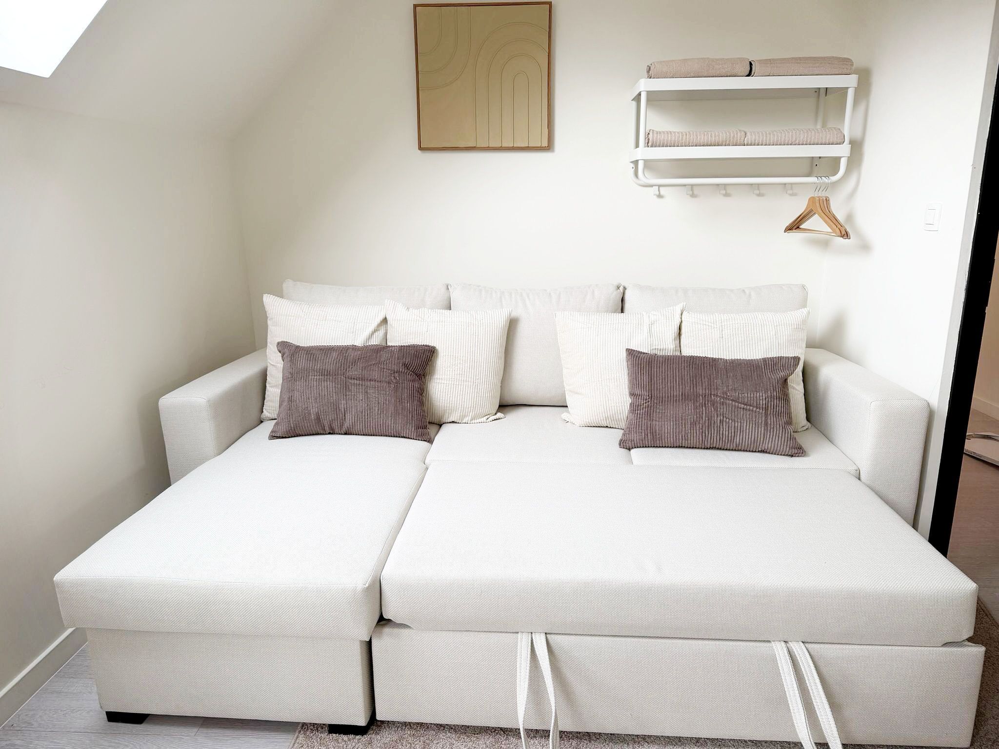 A two-seater sofa with storage drawers, a wall-mounted shelf with towels, and a hanging garment rack.