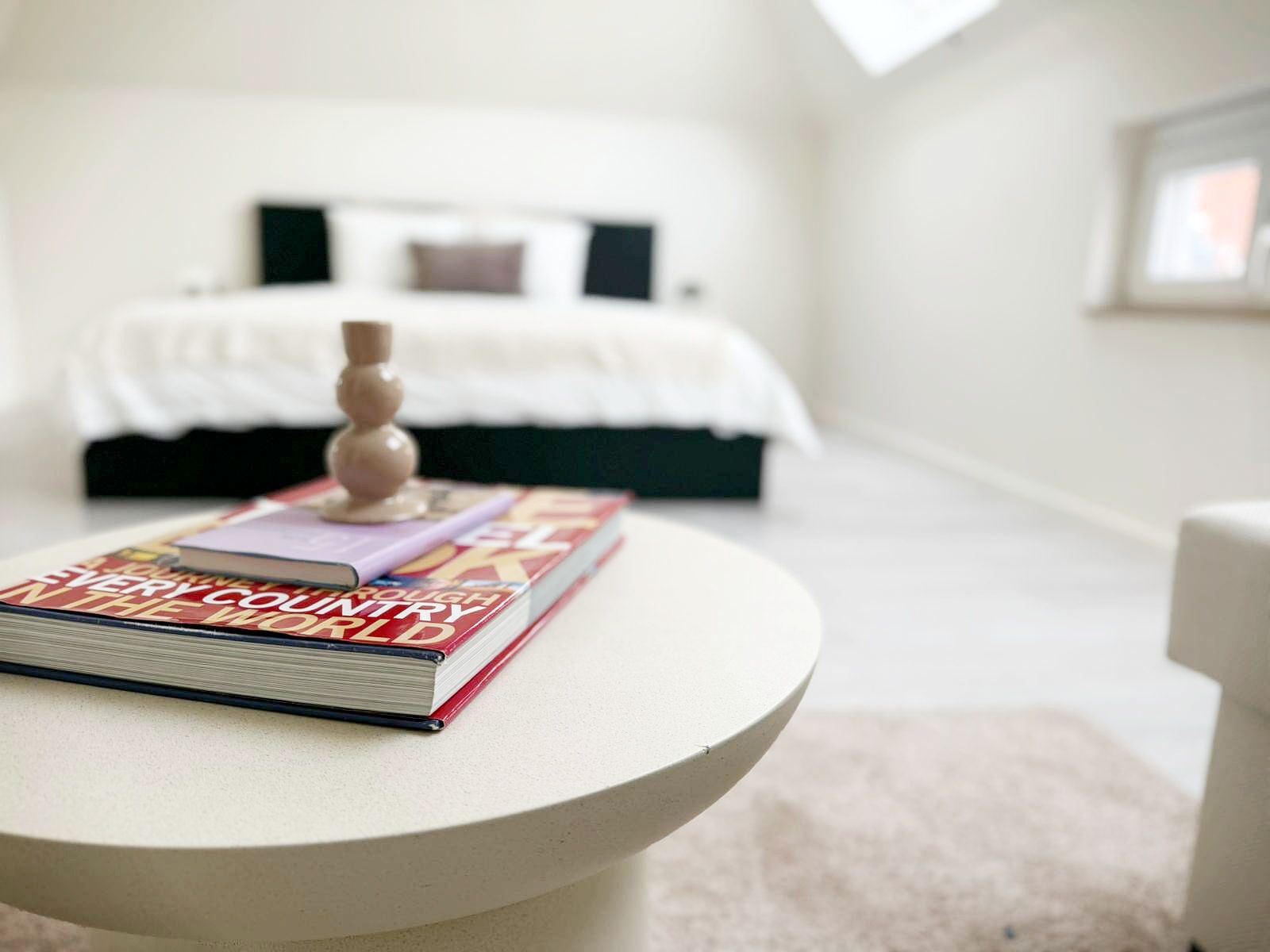 Un dormitorio con cama, una mesita de noche con un libro y una pared blanca.