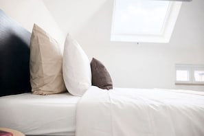 Una cama con ropa blanca y tres almohadas de diferentes texturas y colores.