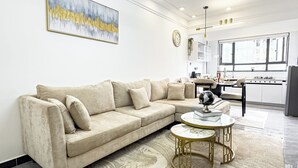 A modern living room with a beige sectional sofa, a round coffee table, and a large abstract painting on the wall. - Neptune Residency (Nairobi)