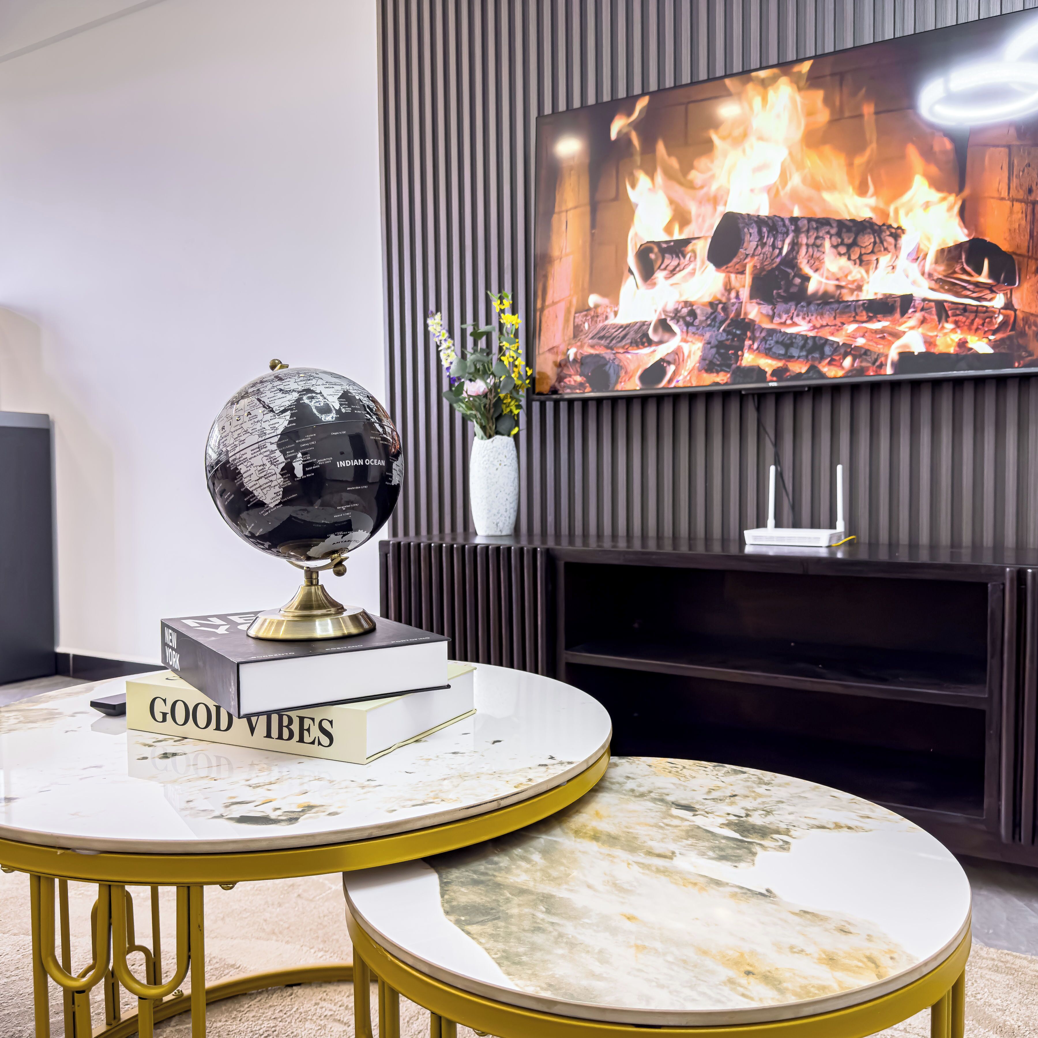 Ein modernes Wohnzimmer mit rundem Tisch, Globus, Büchern, Kamin und Fernseher sowie einer Zierpflanze.