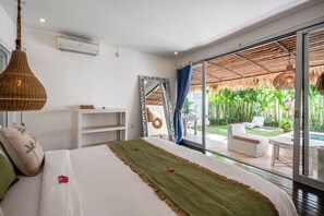 A bedroom with a bed, a bedside table, a mirror, and a view of an outdoor area with a pool and plants. - Maison 246 2BR Cozy Private Pool Villa In Vibrant Canggu (Badung)