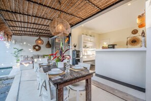 A dining area with a table set for four, a kitchen in the background, and a pool area visible to the left. - Maison 246 2BR Cozy Private Pool Villa In Vibrant Canggu (Badung)