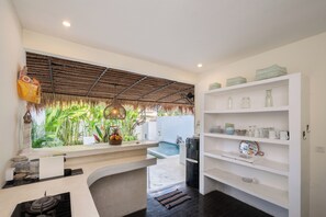 A modern kitchen with a built-in island, white cabinetry, and a view of a pool. - Maison 246 2BR Cozy Private Pool Villa In Vibrant Canggu (Badung)