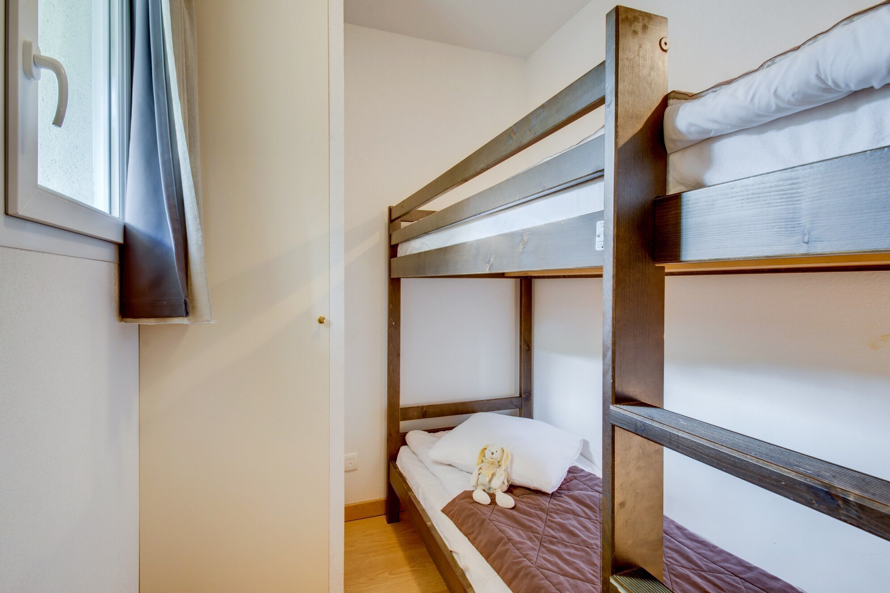 A bunk bed with a window, a wooden door, and a small stuffed toy on the bed.