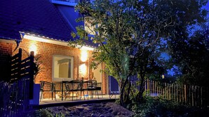 Una casa de ladrillo con un patio, mobiliario exterior y un árbol.