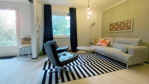 Una sala de estar moderna con un sofá, una silla, una mesita, un tapete a rayas blanco y negro, una ventana con cortinas y una lámpara colgante.