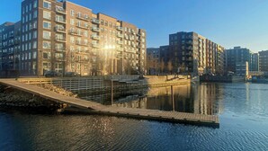 Edificio residenziale sul lungomare, con balconi, un molo e un bacino d'acqua tranquilla.