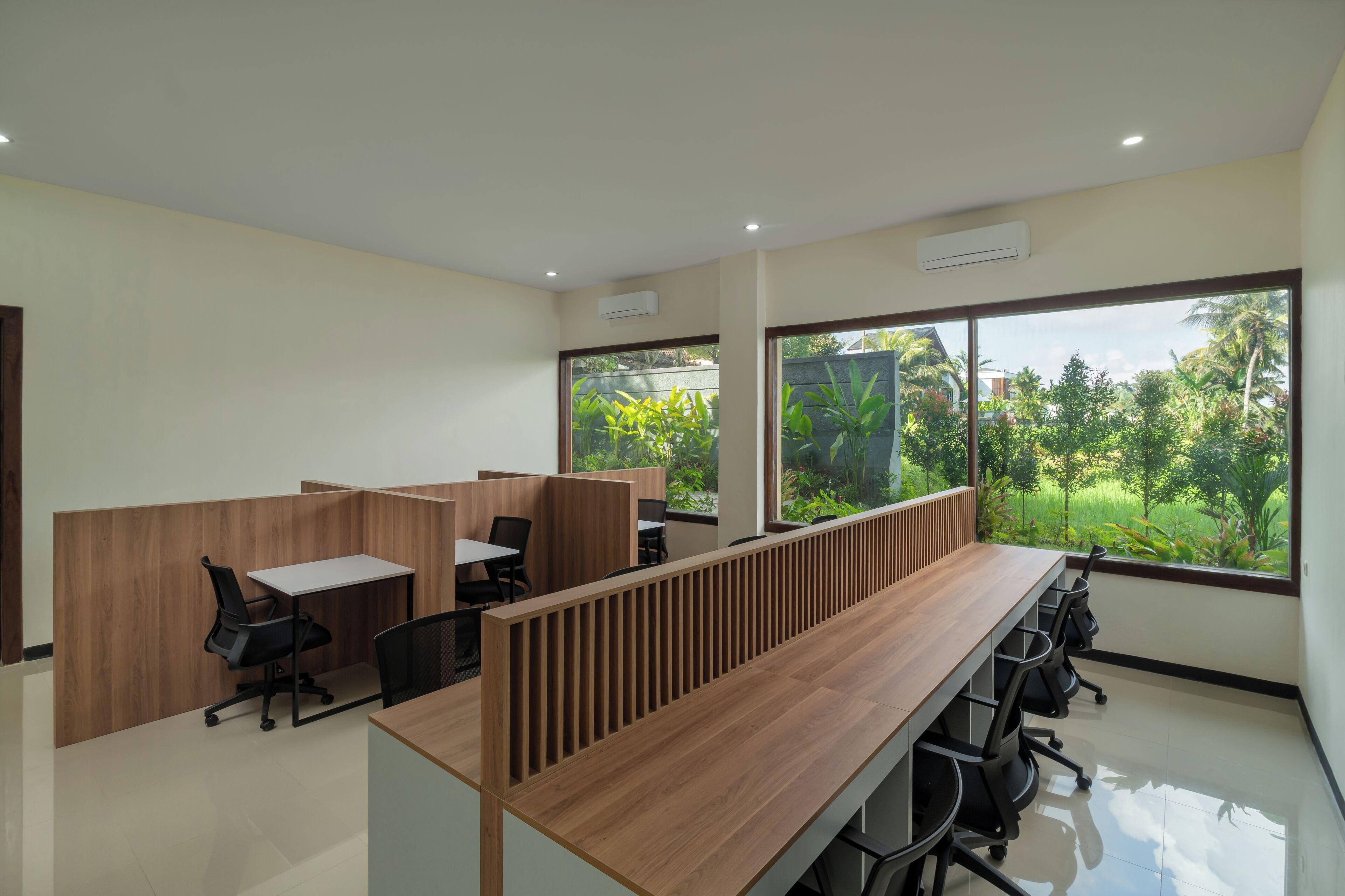 Un espacio de oficina moderno con separadores de madera, puestos de trabajo individuales y amplios ventanales que ofrecen vistas a zonas verdes.