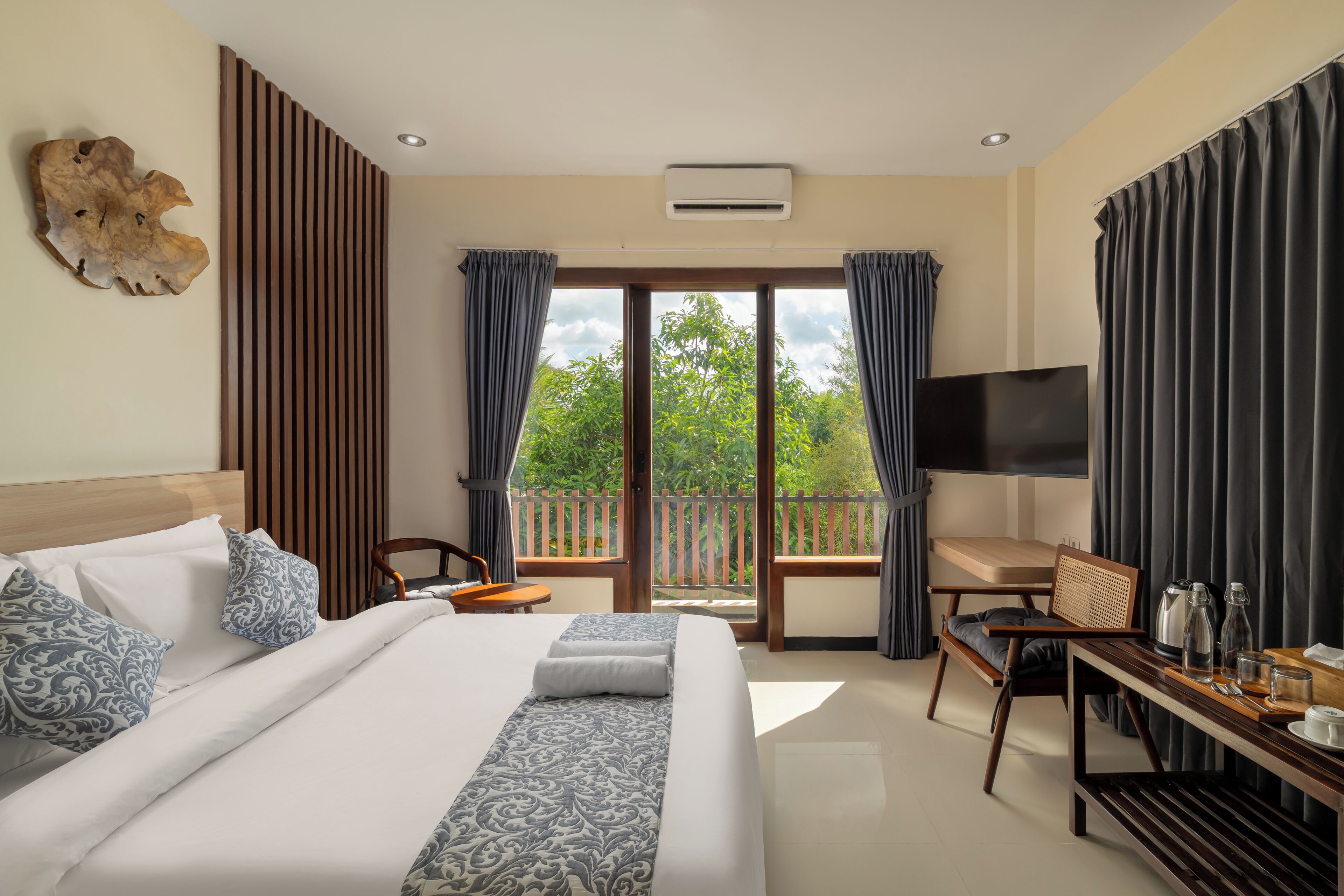 Habitación de hotel con una cama grande, un escritorio, televisión y balcón con vista a zonas verdes.