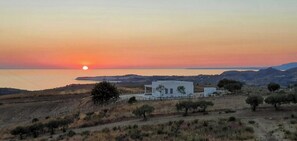 Eine Küstenlandschaft mit Sonnenuntergang, einem weißen Gebäude und spärlicher Vegetation.