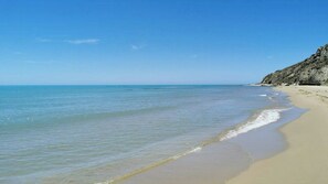 Ein Strand mit klarem Wasser, einem sandigen Ufer und einer felsigen Klippe.