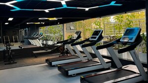 A gym with treadmills, exercise bikes, and a large window with a view of trees. - Neptune Residency (Nairobi)