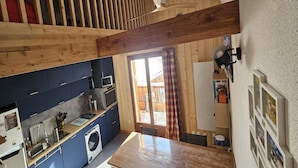 A kitchen with wooden beams, a washing machine, and a dining area with a table. - Alpine Retreat With Balcony and Parking (Saint-Sorlin-d'Arves)