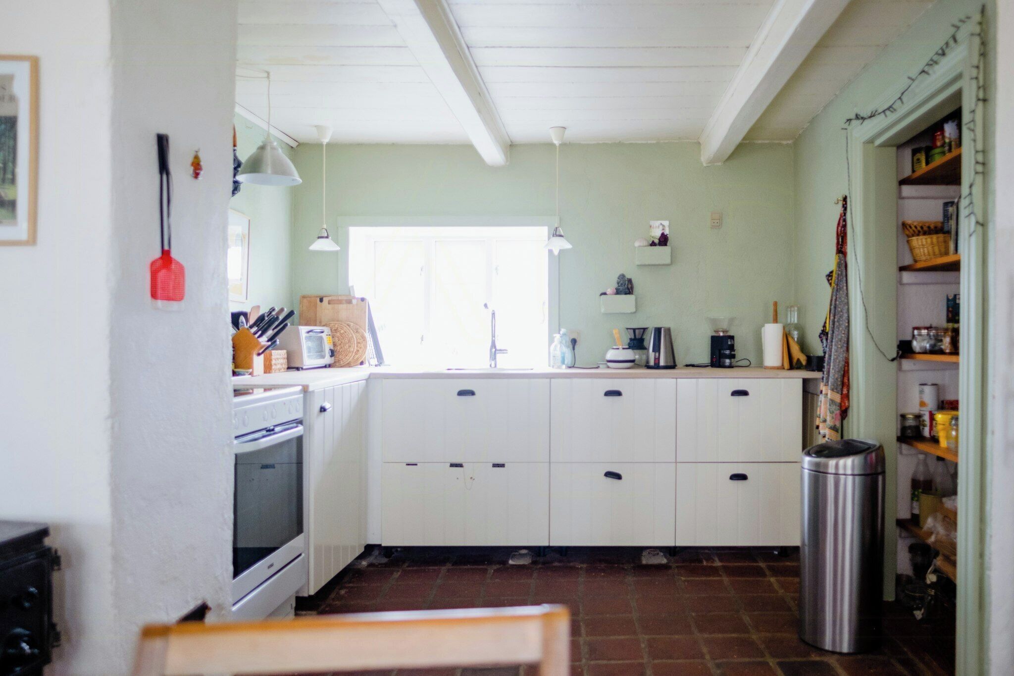 A kitchen with white cabinets, a sink, a stove, and a trash can.