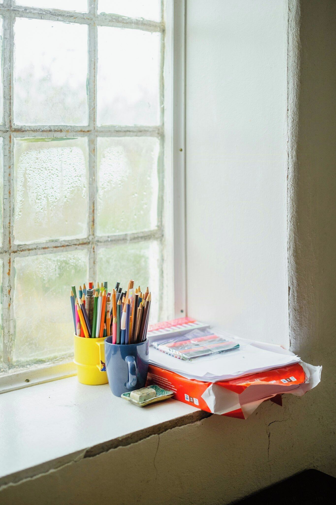 A window sill with a cup of pencils, a book, and a package.
