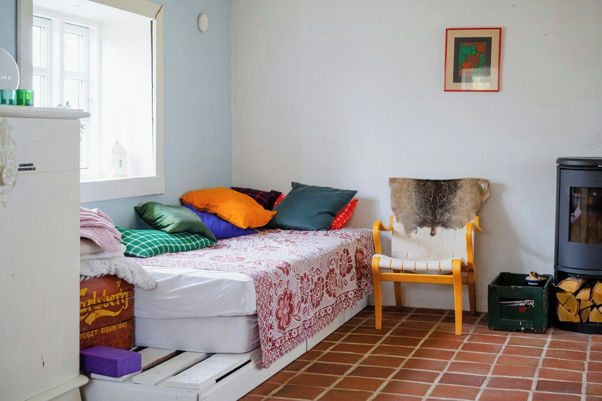 A small, cozy room with a bed, a chair, a fireplace, and a window.