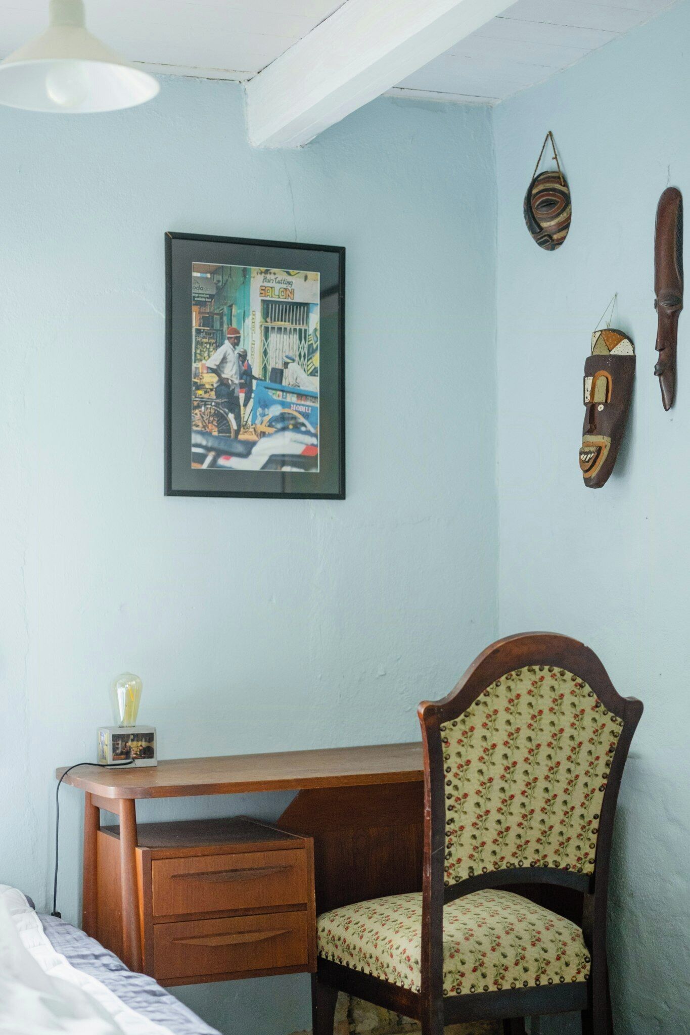 Una habitación con un escritorio de madera, una silla con tapicería floral, un cuadro en la pared y un adorno fijado a la pared.