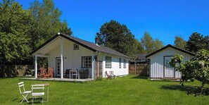 Ein zweistöckiges weißes Haus mit Veranda, einer kleinen Terrasse und einem umzäunten Garten.