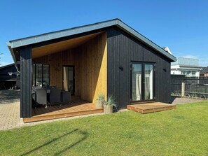 A modern house with a covered patio, a wooden deck, and a large sliding glass door. - Newly renovated house in the middle of Blokhus (Blokhus)