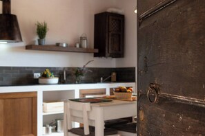 A kitchen with a wooden door, a white table, and a shelf with kitchen items. - Flat at farm stay with spa and pool (Massa Marittima)