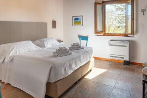 A bedroom with a bed, a chair, a window, and an air conditioning unit. - Flat at farm stay with spa and pool (Massa Marittima)