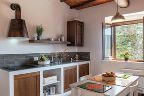 A kitchen with a black countertop, wooden cabinets, a hanging light, and a window with a view of trees. - Flat at farm stay with spa and pool (Massa Marittima)